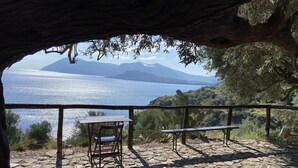 A rustic outdoor seating area with a table and chairs, overlooking a body of water and distant mountains. - House "sole" - Unique Panorama (Lipari)