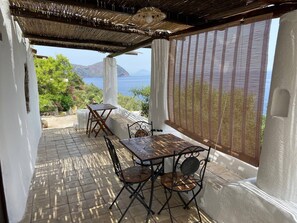 A covered outdoor patio with a table and chairs, a view of the sea, and a pergola structure.