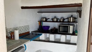 Eine kompakte Küche mit Kühlschrank, Mikrowelle und Regalen für Töpfe und Pfannen.