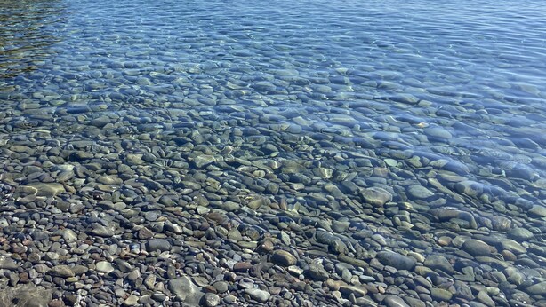 Ein freier Blick auf eine felsige Küste mit ruhigem Wasser und einem entfernten Boot.