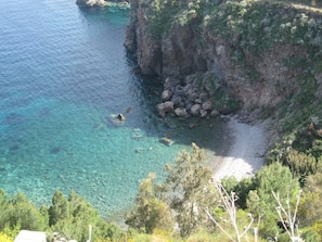 A coastal landscape with clear blue waters, rocky cliffs, and dense greenery.