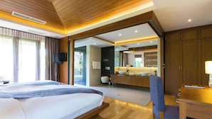 Ein Schlafzimmer mit Bett, Schreibtisch, Stuhl, Fernseher und einem durch eine offene Tür einsehbaren Badezimmer.
