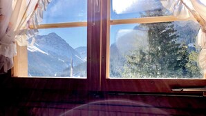 Une chambre à coucher avec une tête de lit en bois, une fenêtre donnant sur des montagnes enneigées et un lit recouvert d’une literie à motifs floraux.