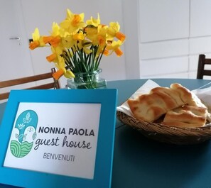 Une table avec une pancarte bleue sur laquelle on peut lire « NONNA PAOLA, chambre d’hôtes », et un panier de pain.