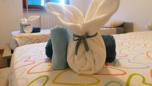 Une chambre avec un lit agrémenté d’une couverture aux motifs de cœurs colorés, une serviette blanche ornée d’un nœud et une serviette bleue.