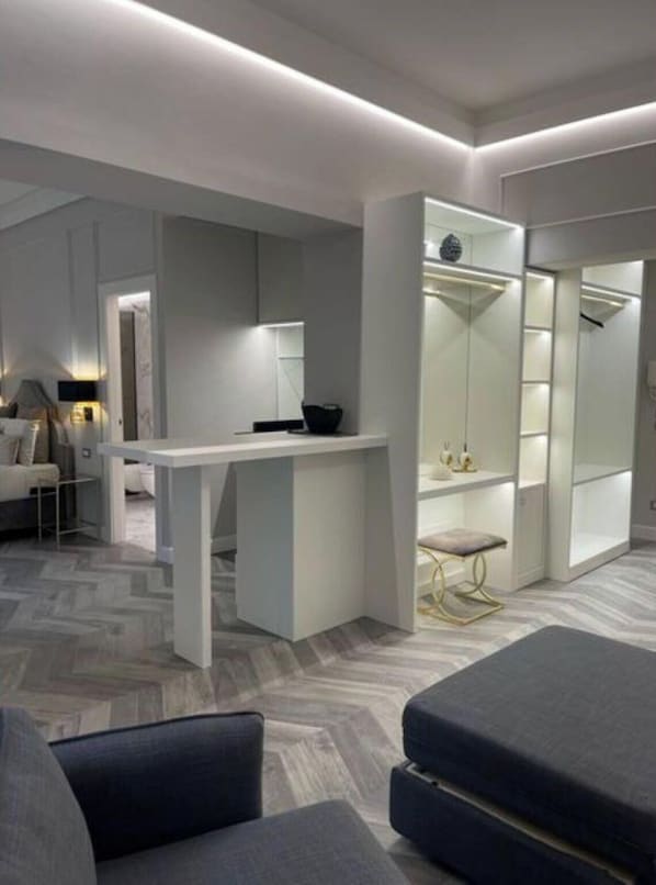 A modern hotel room with a central seating area, a small table, and a walk-in closet with mirrored doors.