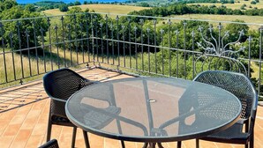 Een terras met een tafel en stoelen, met uitzicht op een schilderachtig landschap met bergen en een waterpartij.