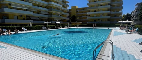 Una piscina con suelo de baldosas, rodeada de edificios amarillos con balcones.