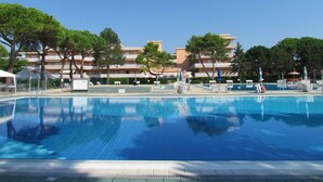 A swimming pool with tiled flooring, surrounded by trees and a multi-story building with balconies. - Enjoy a Comfy Flat With Shared Pool - Beahost (San Michele al Tagliamento)