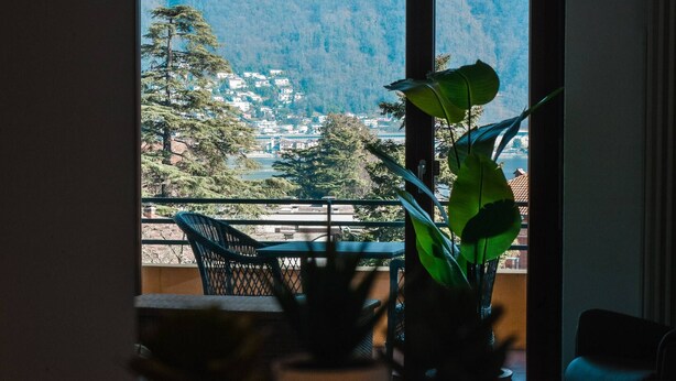 A balcony with a view of a mountainous town, a potted plant, and a chair. - Vacation Rental Seeblick Pocobelli in Melide (Melide)