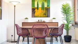 A dining area with a wooden table, two red chairs, a floor lamp, a painting, and a potted plant. - Vacation Rental Seeblick Pocobelli in Melide (Melide)