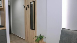 A hallway with a wooden panel wall, a mirror, a small round table with a plant, and a grey sofa. - New Deluxe Studio 1 - Downtown Thessaloniki-fully Equipped (Thessaloniki)