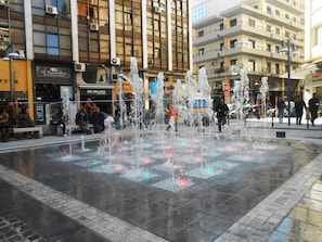 A public square with a water fountain and surrounding buildings.