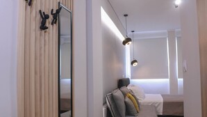 A modern hotel room with a wooden panel wall, a bed with multiple pillows, a bedside table, and a hanging light fixture. - New Deluxe Studio 1 - Downtown Thessaloniki-fully Equipped (Thessaloniki)