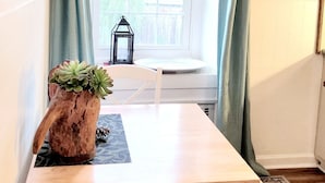 A dining area with a wooden table and white chairs, a potted succulent on the table, and a view of a wooden deck through a window with green curtains. - ext Stay, the Design Apt, Sanctuary of the Swan Wellness Hotel Swan Rescue (Birdsboro)