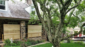 A stone house with a covered porch, a tree in the yard, and a statue of a Buddha. - ext Stay, the Design Apt, Sanctuary of the Swan Wellness Hotel Swan Rescue (Birdsboro)