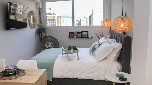 Un dormitorio con cama, mesita de noche, silla y ventana con vistas a la ciudad.
