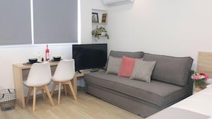 A modern living room with a grey sofa, two white chairs, a flat-screen TV, a small table with a bowl and bottle, and a plant. - New Studio 4 Downtown Thessaloniki-fully Equipped (Thessaloniki)