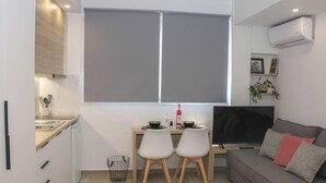A compact living space with a kitchenette, a dining area with two chairs, a TV, and a sofa with cushions. - New Studio 4 Downtown Thessaloniki-fully Equipped (Thessaloniki)