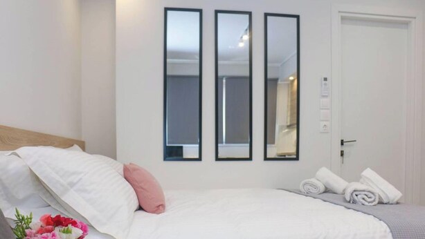A hotel room with a bed, a wall-mounted mirror, a door, and a small table with towels. - New Studio 4 Downtown Thessaloniki-fully Equipped (Thessaloniki)