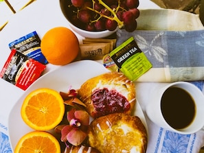 A breakfast setting with pastries, fruit, tea bags, and a cup of coffee.