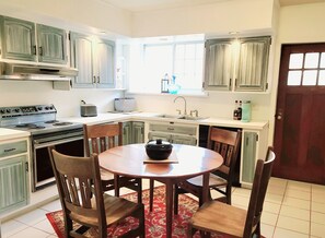 A kitchen with a stove, sink, and dining area with chairs.