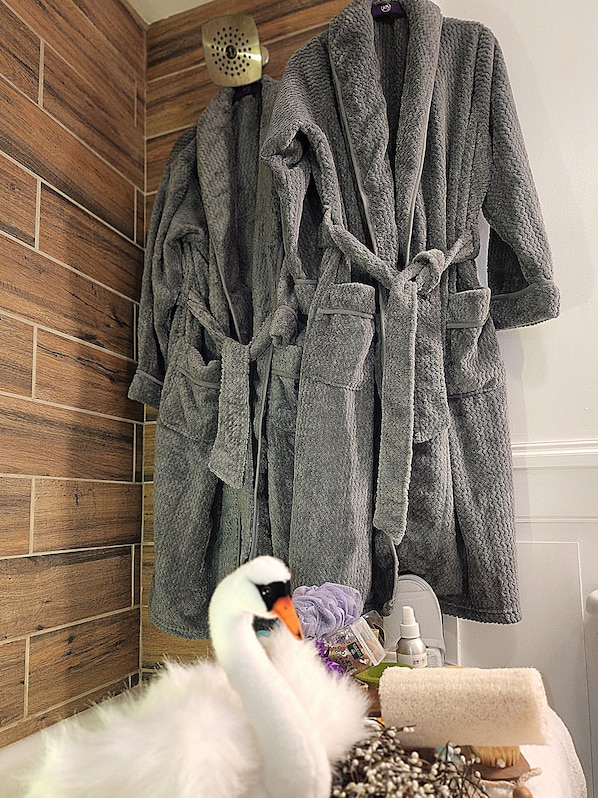 A bathroom with wooden wall tiles, a white fluffy object, a swan figurine, and two gray bathrobes hanging on the wall.