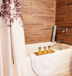 A bathroom with a wooden wall, a bathtub, and three toiletries on a tray.