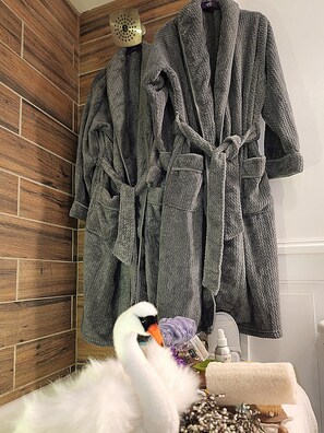 A bathroom with wooden wall tiles, a white fluffy object, a swan figurine, and two gray bathrobes hanging on the wall.