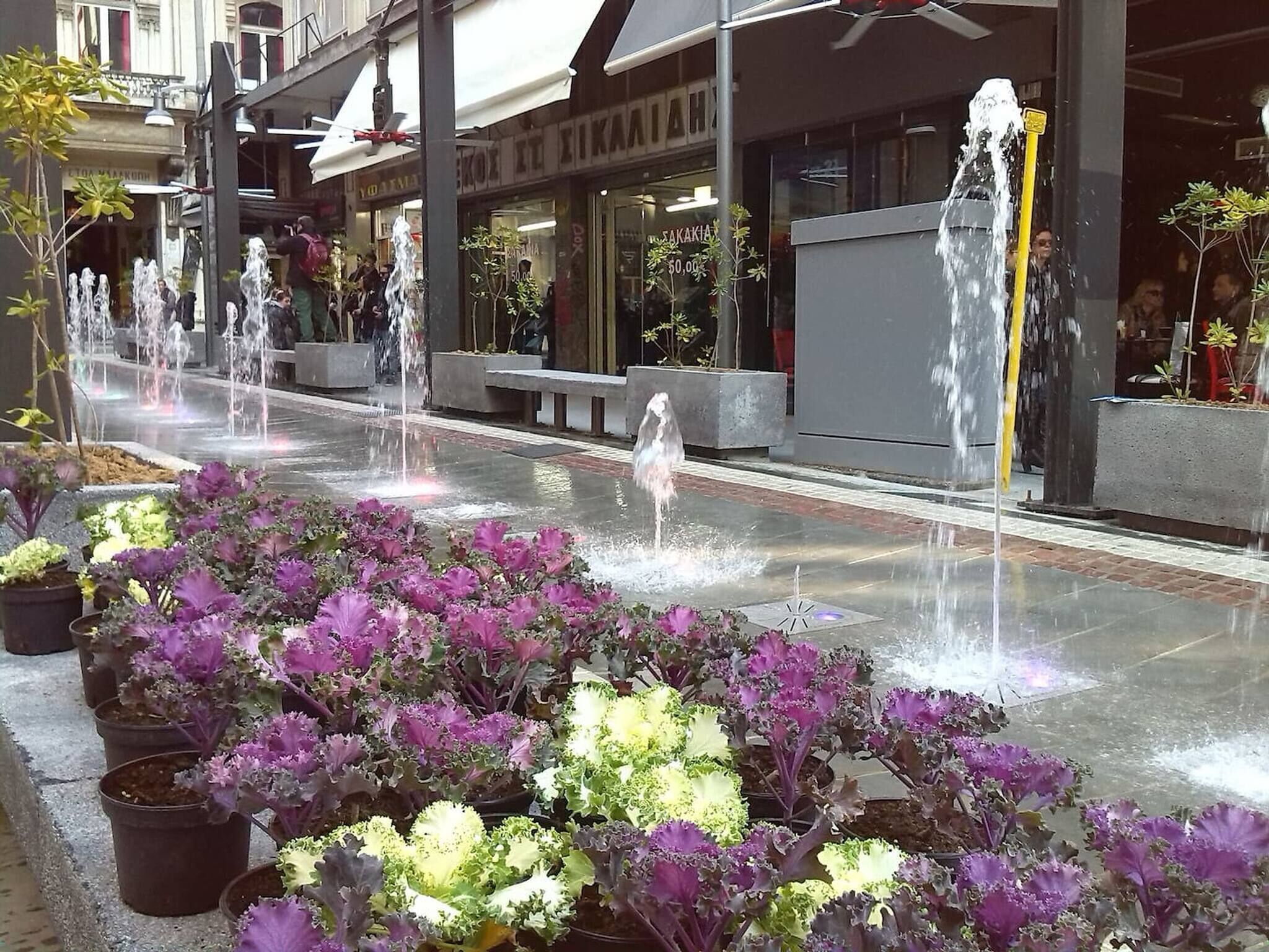 A public square with multiple fountains and potted plants.