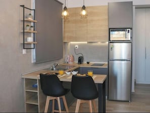 A modern kitchen with a stainless steel refrigerator, a microwave, a kettle, and two black chairs at a wooden table.