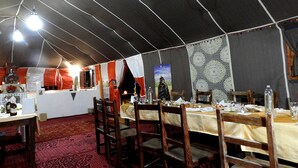 Un comedor con toldo, mesas dispuestas para comidas, sillas de madera y una alfombra estampada.