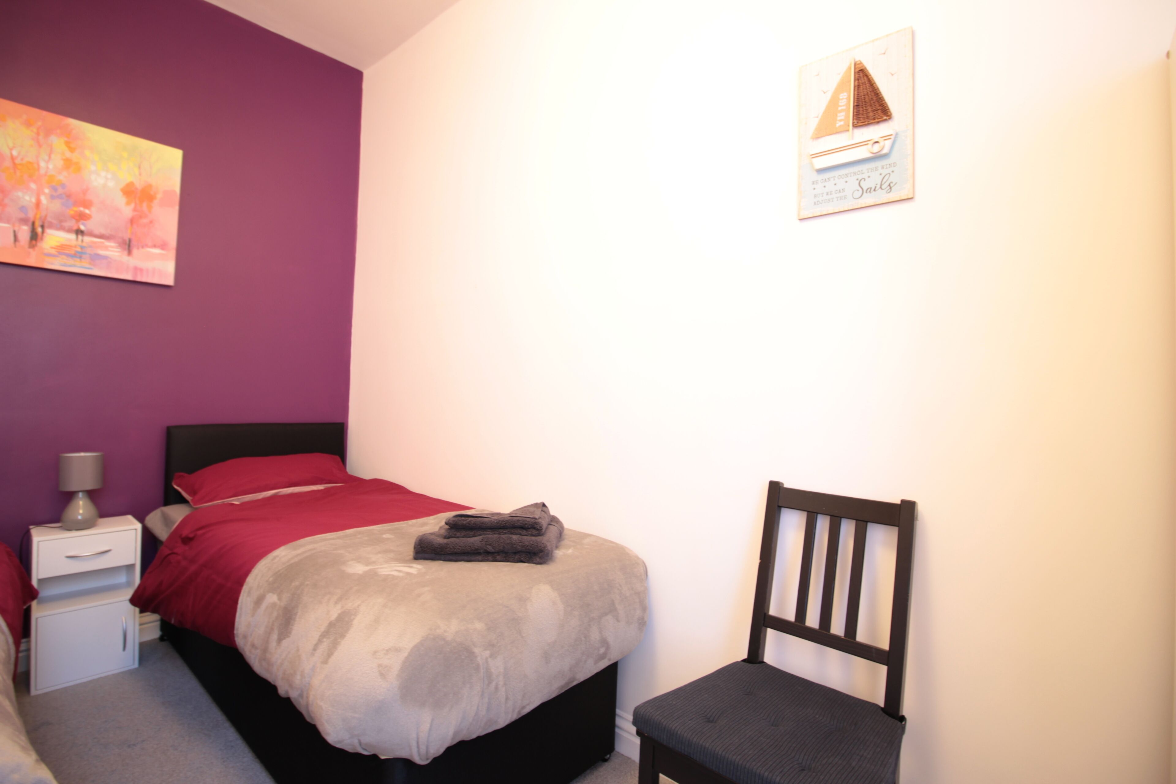 A bedroom with a bed, a chair, a nightstand, and a wall painting.