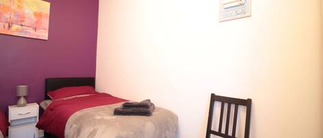 A bedroom with a bed, a chair, a nightstand, and a wall painting.