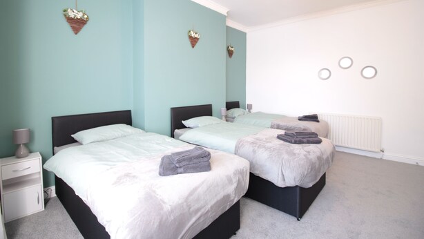 A bedroom with two beds, a nightstand, a lamp, and a radiator. - Lovely 2-bed Downstairs Apartment (Gateshead)