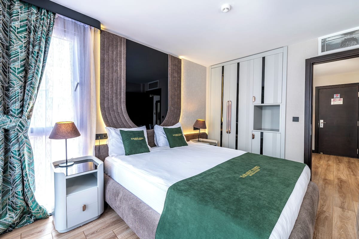 Quarto de hotel com cama, mesas de cabeceira, guarda-roupa e porta.