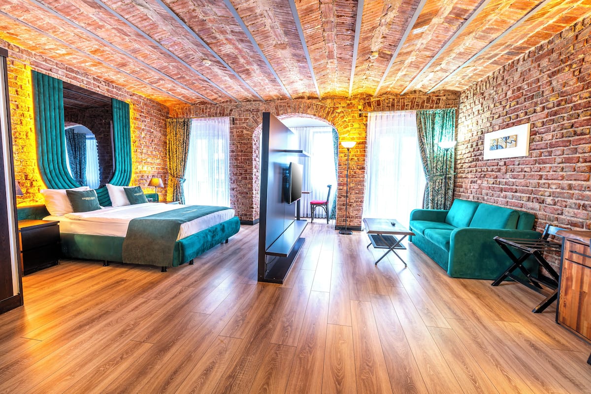 Quarto com parede de tijolos, piso de madeira, cama, sofá, escrivaninha e espelho.