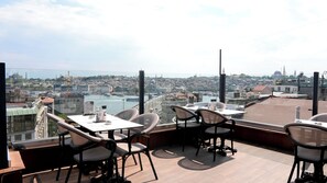 A rooftop terrace with tables and chairs, offering a view of a cityscape with buildings and a body of water. - Karakoy Aparts Hotel (Istanbul)