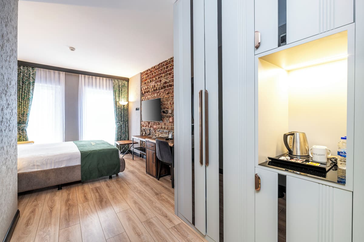 Quarto de hotel com uma cama, uma escrivaninha, televisão e kitchenette.