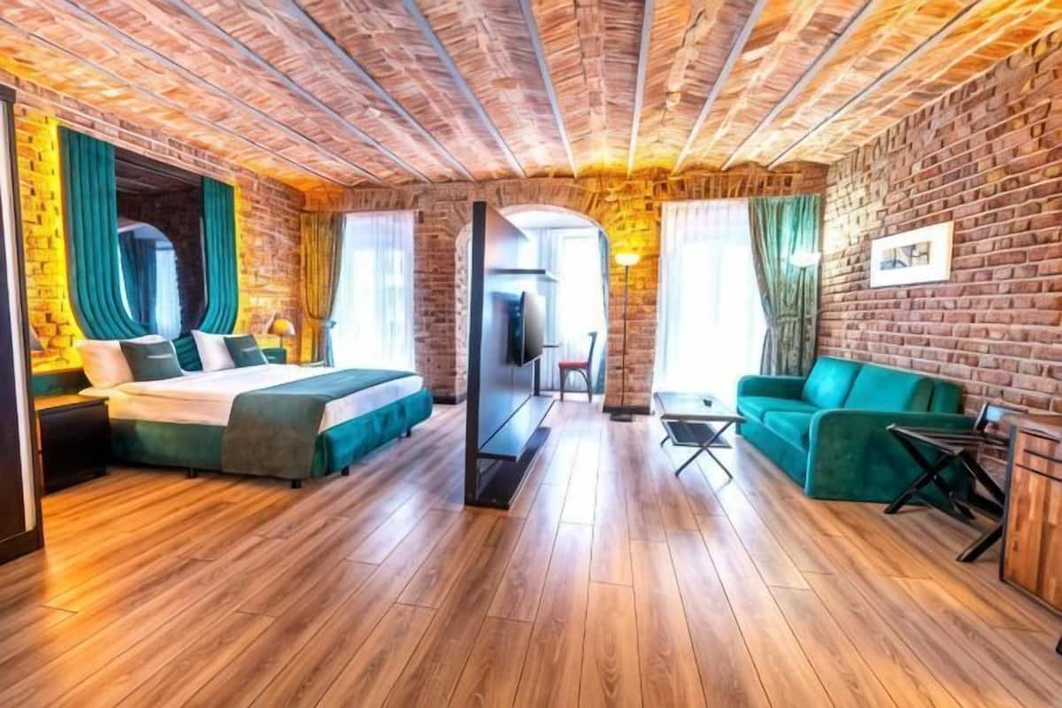 Quarto com parede de tijolos, piso de madeira, cama, sofá e televisão.