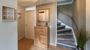 Un couloir avec un meuble en bois, un miroir, un présentoir à clés et un escalier.