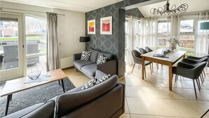Un salon moderne avec un canapé gris, une table à manger et des chaises, et une vue sur un canal à l’extérieur.