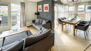 Een moderne woonkamer met een grijze bank, een eettafel met stoelen en een uitzicht op een gracht.