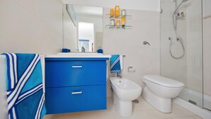 A modern bathroom with a blue vanity, a white toilet, a bidet, and a glass-enclosed shower area. - Villa Mariuccia Apartment Bea J (Capri)