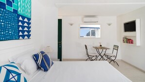 A hotel room with a bed, a desk with two chairs, a TV, and a bookshelf. - Villa Mariuccia Apartment Bea J (Capri)