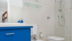 A modern bathroom with a blue vanity, a bidet, a toilet, and a glass-enclosed shower. - Villa Mariuccia Apartment Bea J (Capri)