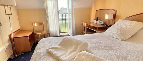 Habitación de hotel con una cama grande, un escritorio, una silla, una mesita de noche y vistas al exterior a través de una ventana.