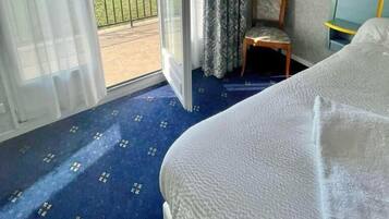 Ein Hotelzimmer mit Bett, Sessel, Schreibtisch und Blick auf eine grüne Landschaft durch eine Schiebetür.