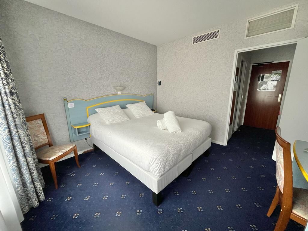 A neatly arranged hotel room with a large bed, a chair, a small table, and a door.