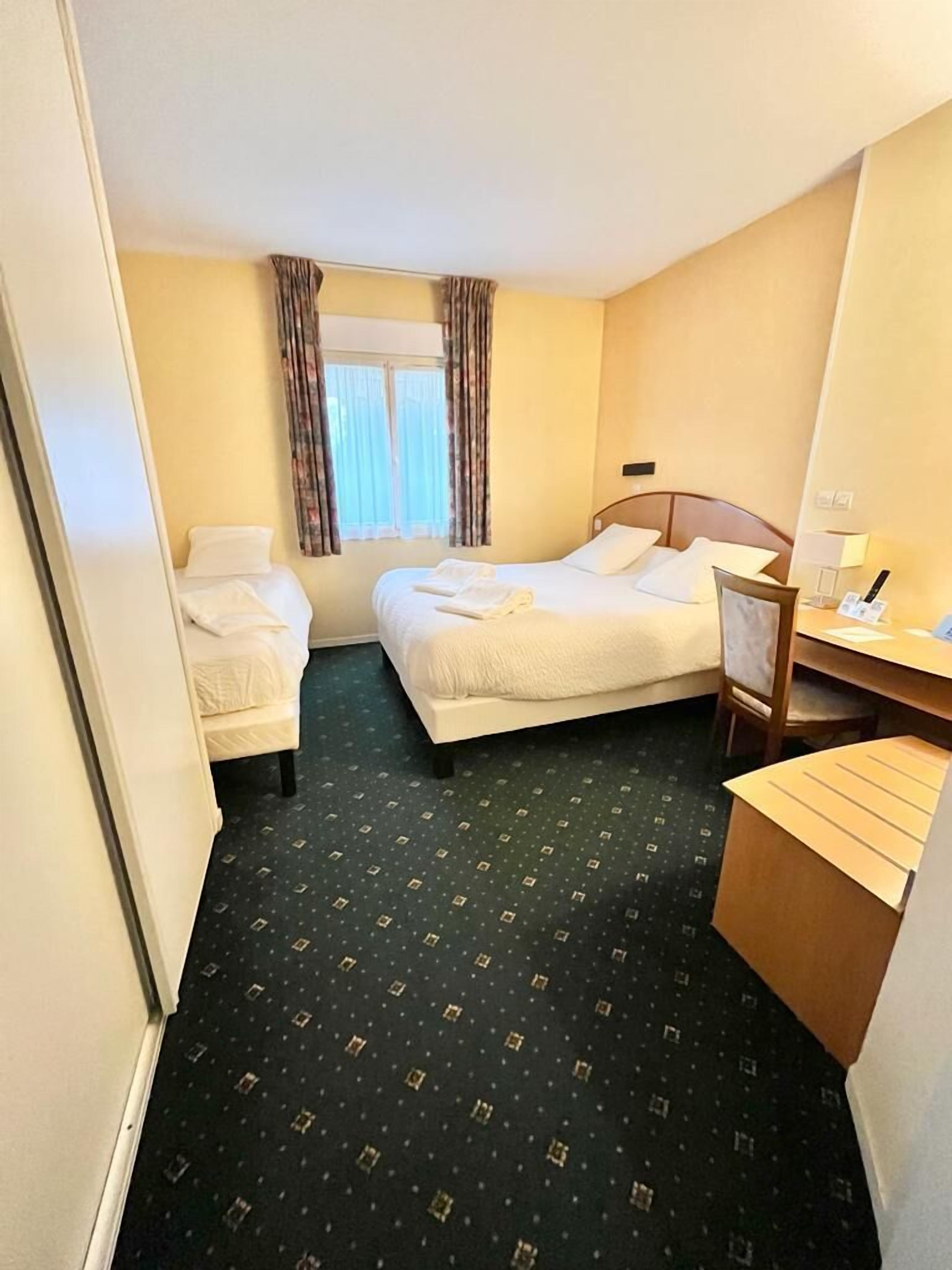 Une chambre d’hôtel avec deux lits, un bureau et une chaise.